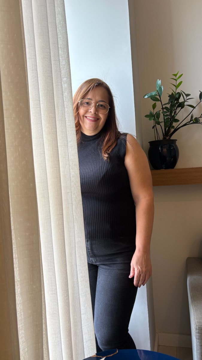 Silvane Abreu em pé, em ambiente com luz natural e uma planta ao fundo.